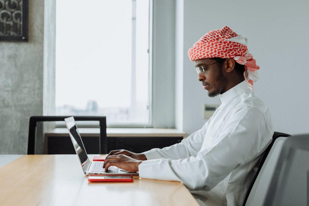 Middle Eastern man focused on work at a modern office desk with a laptop.